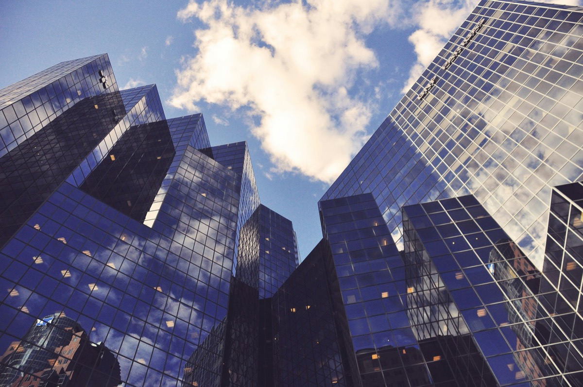 Looking up at glass office towers reflecting sky and cloud